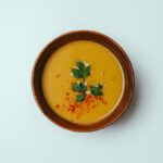 Top view of fresh pumpkin cream soup decorated with herbs and paprika served in bowl on white background in room