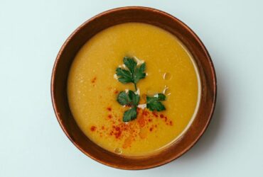 Top view of fresh pumpkin cream soup decorated with herbs and paprika served in bowl on white background in room